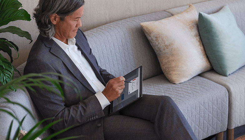 Eine Person sitzt auf einem Sofa und unterschreibt mit dem Surface Slim Pen 2 auf dem Surface Pro 8