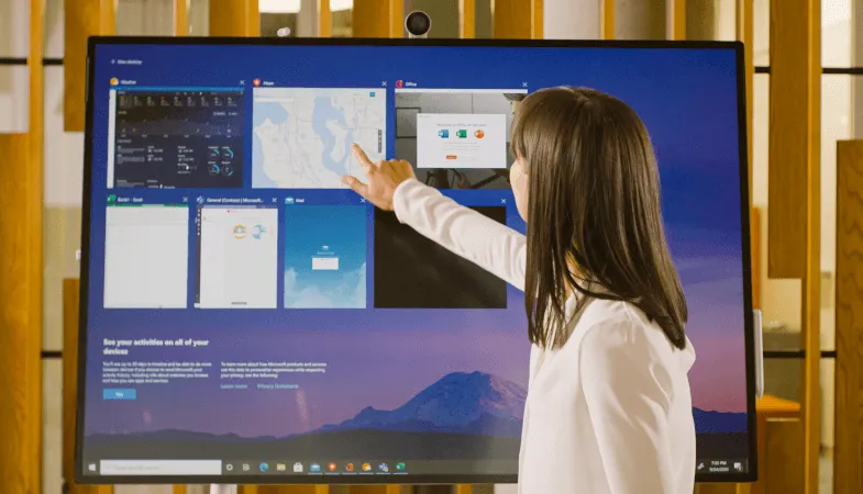 A woman works on the Surface Hub 2S 50 inch, the Surface Hub 2S Fingerprint Reader is visible on the left side of the Hub 