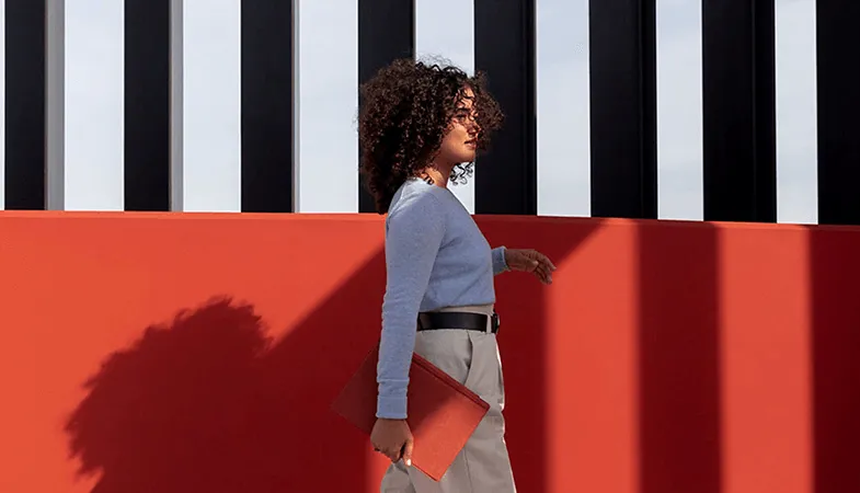 A woman walks in front of a building with a Surface Pro including poppy-red Type Cover in her hand