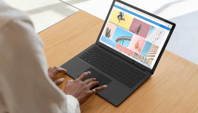 A woman is typing on the Surface Laptop in black, which stands on a table 