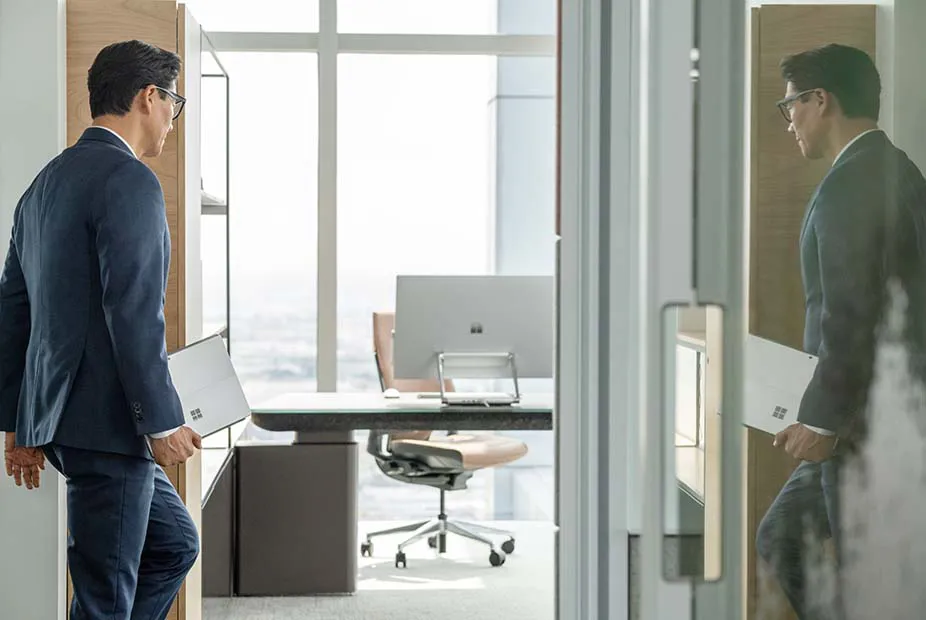High resolution video calls in HD and 4K, improved meeting experience and background noise suppression A man carries a Surface Pro 9 into a meeting room