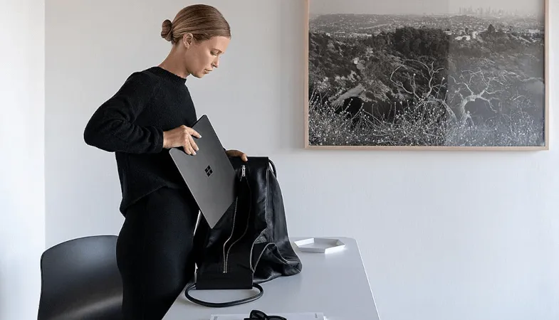 Eine Frau steht am Schreibtisch und packt ihren Surface Laptop in die Tasche