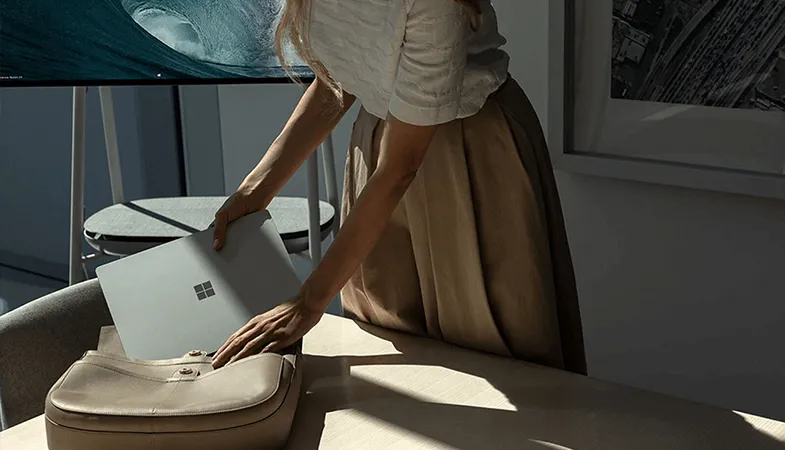 Eine Frau packt ihren Surface Laptop in ihre Tasche, die auf einem Tisch liegt 