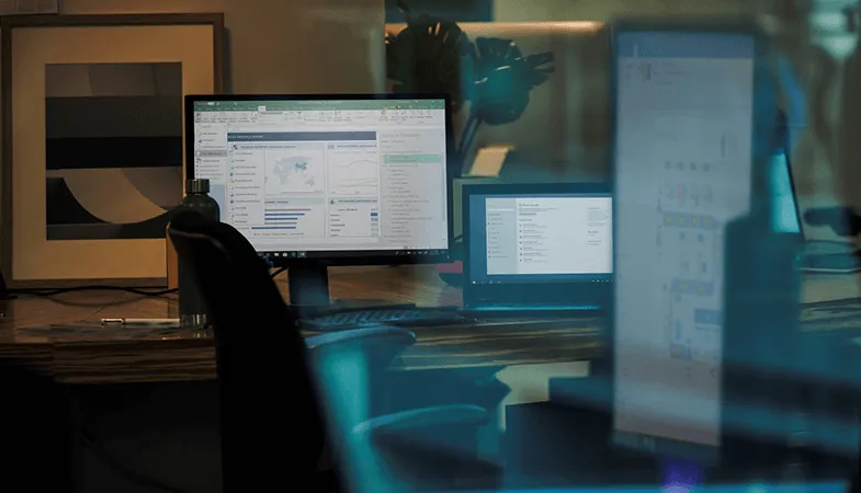 Ein Schreibtisch mit mehreren Bildschirmen, auf denen Microsoft Office-Anwendungen zu sehen sind