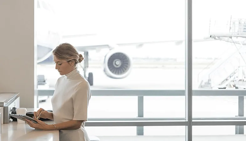 Mit Microsoft 365 Dokumente von jedem Ort der Welt abrufen Eine Frau sitzt am Flughafen und arbeitet am Surface Pro