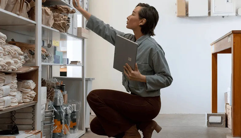 A woman arranges products on a storage shelf and organises them using the Surface Pro 
